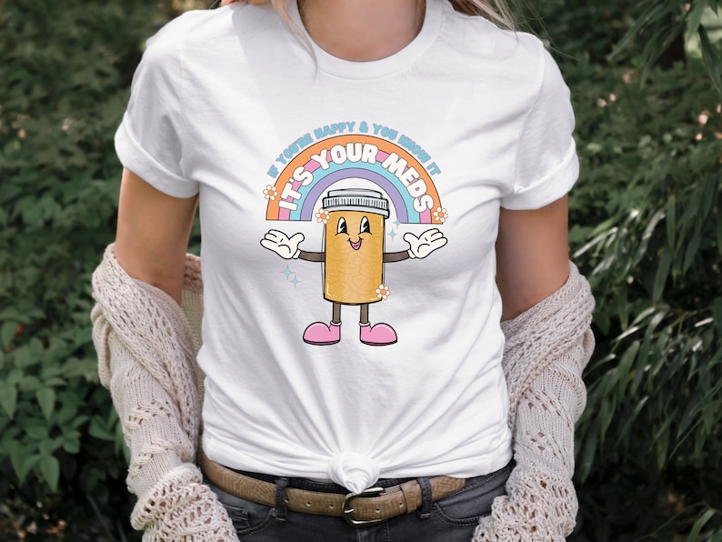 Peut inclure: T-shirt blanc avec un arc-en-ciel et une pilule de dessin anim&eacute; avec le texte "Si vous &ecirc;tes heureux et que vous le savez, c'est vos m&eacute;dicaments".