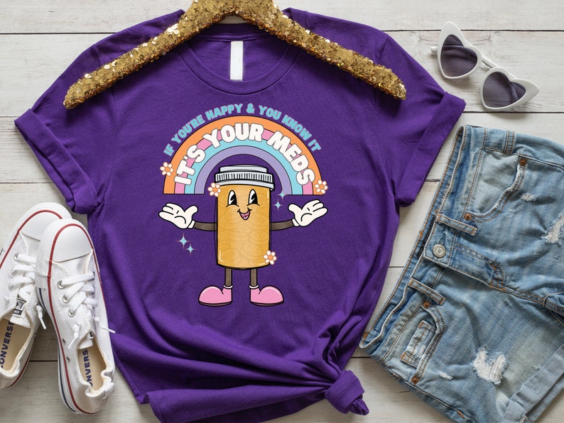 Peut inclure: T-shirt violet avec un arc-en-ciel et une pilule de dessin anim&eacute; avec le texte "Si vous &ecirc;tes heureux et que vous le savez, c'est vos m&eacute;dicaments".