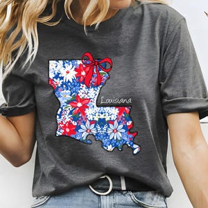 May include: A gray t-shirt with a floral print of the state of Louisiana. The print includes a red bow and the word "Louisiana".