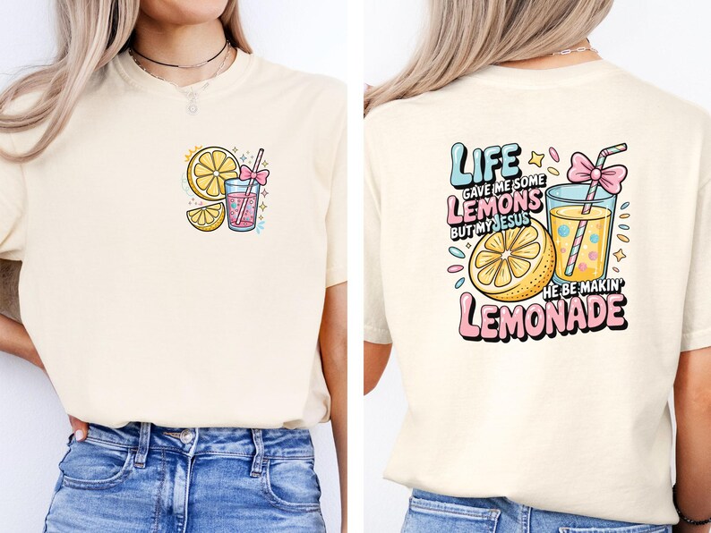 May include: Cream-colored t-shirt with a colorful lemonade-themed graphic. The front features a lemon slice, a drink with a straw, and the text "Life gave me some lemons." The back has the text "Life gave me some lemons but my Jesus he be makin' lemonade."