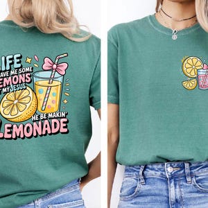 May include: Teal t-shirt with a colorful graphic featuring a lemon, a glass of lemonade, and the text "Life gave me some lemons but my Jesus he be makin' lemonade." The design includes pink and yellow accents.