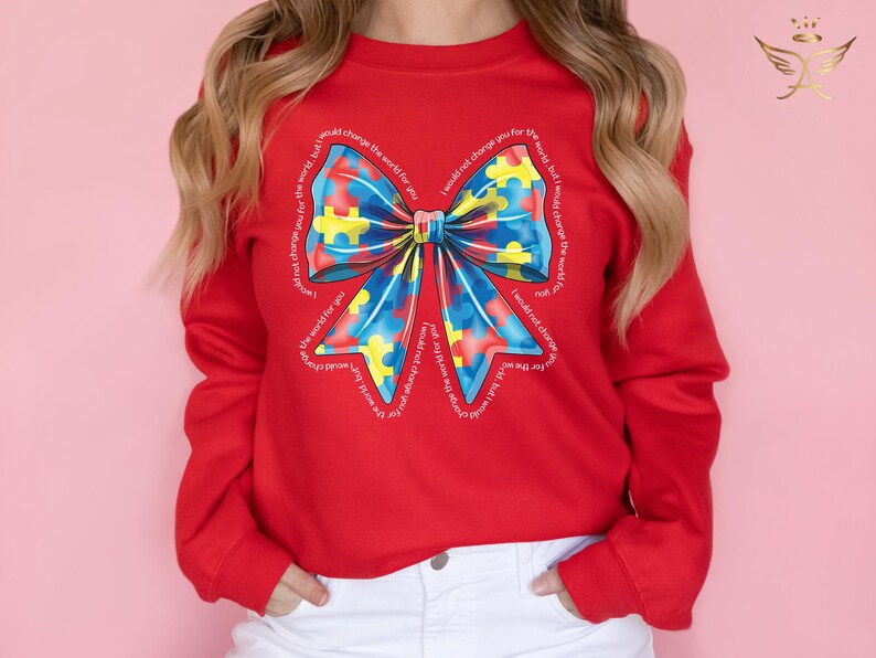 Puede incluir: Sudadera roja con un gran lazo azul, amarillo y rojo hecho de piezas de rompecabezas. El lazo est&aacute; rodeado por el texto "No cambiar&iacute;a el mundo por ti, pero cambiar&iacute;a el mundo por ti".