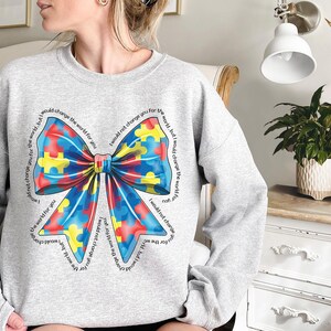 Puede incluir: Sudadera gris con un lazo de piezas de rompecabezas azul, amarillo y rojo. El texto alrededor del lazo dice "No te cambiar&iacute;a por el mundo, pero cambiar&iacute;a el mundo por ti".