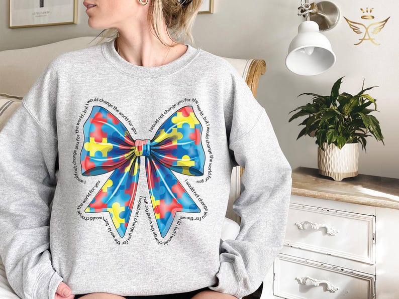 Puede incluir: Sudadera gris con un lazo de piezas de rompecabezas azul, amarillo y rojo. El texto alrededor del lazo dice "No te cambiar&iacute;a por el mundo, pero cambiar&iacute;a el mundo por ti".