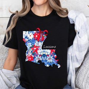 May include: Black t-shirt with a floral print of the state of Louisiana. The print includes a red bow and the word "Louisiana".