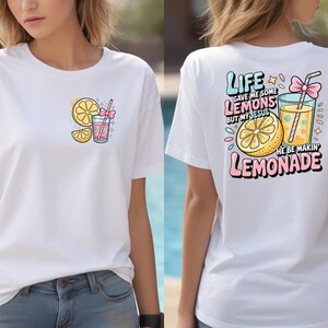 May include: White t-shirt with a colorful lemon and lemonade graphic. The front features a lemon slice and a drink with a straw. The back has the text "Life gave me some lemons but my Jesus he be makin' lemonade."