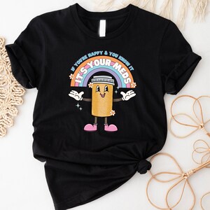 Peut inclure: T-shirt noir avec un arc-en-ciel et une pilule de dessin anim&eacute; avec le texte "Si vous &ecirc;tes heureux et que vous le savez, c'est vos m&eacute;dicaments".