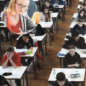 May include: A classroom setting with students taking a test. The students are sitting at desks with papers in front of them. Some students are looking at their papers, while others are looking around the room. There is a woman in the foreground wearing a red shirt and glasses.