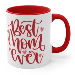 Puede incluir: Taza de caf&eacute; de cer&aacute;mica blanca con borde y asa rojos. La taza tiene una inscripci&oacute;n roja que dice "Best Mom Ever" con peque&ntilde;os corazones rosas.