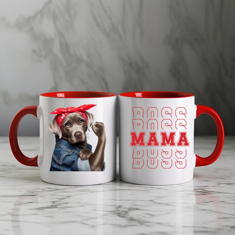 Puede incluir: Dos tazas de cer&aacute;mica blanca con bordes rojos. Una taza presenta un perro marr&oacute;n y gris con un pa&ntilde;uelo rojo y una chaqueta vaquera con el pu&ntilde;o en alto. La otra taza tiene el texto "BOSS MAMA BOSS" repetido en rojo.