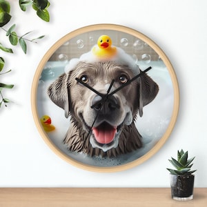 May include: A gray dog with a yellow rubber duck on its head is in a bathtub full of bubbles. The dog is smiling and looking at the camera. The image is on a round wooden clock.