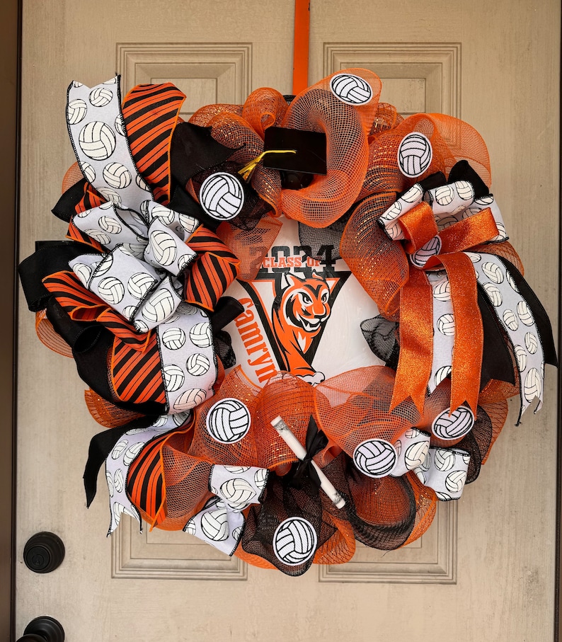May include: A decorative volleyball-themed wreath with orange, black, and white ribbons and mesh. The wreath features volleyball accents and a central design with a tiger mascot and the text "Class of 2024".