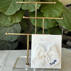 May include: White fabric bow with blue embroidery that says "Royals" on a white card with the text "Happy Day Designs Kansas City, MO".