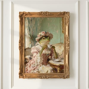 Może przedstawiać: Oprawione dzieło sztuki przedstawia żabę w różowej sukience i kapeluszu w kwiaty, pijącą herbatę. Żaba siedzi przy małym stoliku, trzymając filiżankę herbaty. Ozdobna złota rama dodaje scenie elegancji.