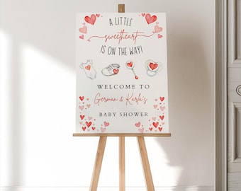 May include: A white sign with red hearts and the text "A little sweetheart is on the way!"  Welcome to German & Karfa's Baby Shower.