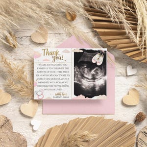 May include: A pink baby shower thank you card with an ultrasound image and text. The card features a pink envelope, decorative hearts, and dried plants. The card reads "Thank you!" and includes a message about celebrating the arrival of a baby.