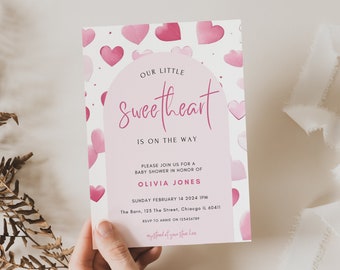 Puede incluir: Una invitación a un baby shower con un diseño de corazones rosas y blancos. El texto dice "Our Little Sweetheart Is On The Way" e incluye detalles para el baby shower de Olivia Jones, incluyendo la fecha, hora y lugar.