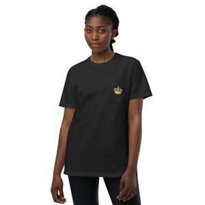 May include: Black t-shirt with a pocket featuring a gold embroidered crown design. The shirt is a classic crew neck style.