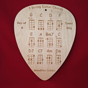 May include: A wooden guitar pick-shaped sign with engraved 3-string guitar chords. The sign includes chord diagrams for G, C, D, F, E, A, Bm7, C, D7, C7, Am, and Em, with the text "3 String Guitar Chords" and "WoodPort Guitars".