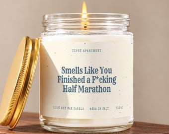 May include: A clear glass jar candle with a gold lid and a lit wick. The label features the text "TIPSY APARTMENT" and "Smells Like You Finished a F*cking Half Marathon" in blue, along with "100% SOY WAX CANDLE", "MADE IN CALI", and "T1141".