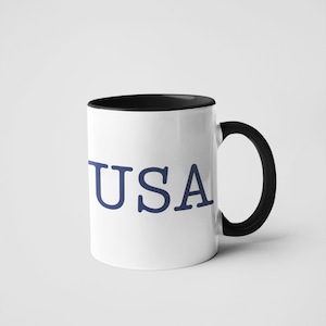May include: A white coffee mug with a black rim and handle. The mug has the word 'USA' printed on the front in blue.