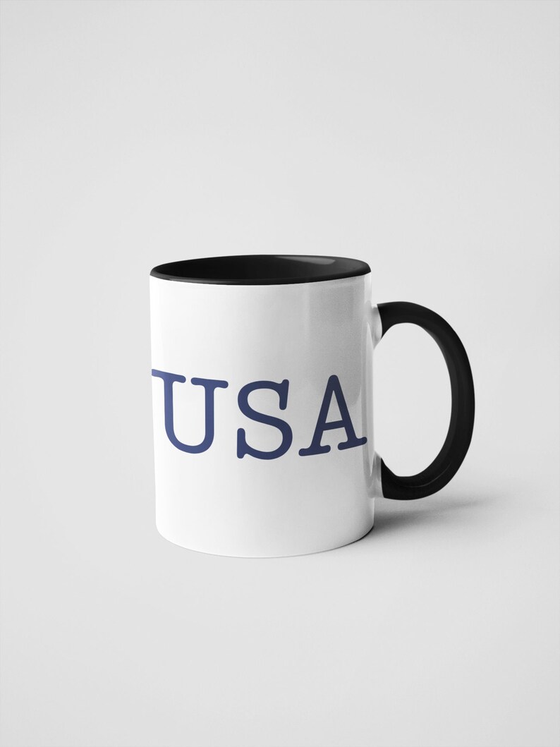 May include: A white coffee mug with a black rim and handle. The mug has the word 'USA' printed on the front in blue.