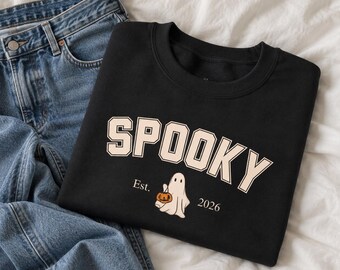 May include: A black crewneck sweatshirt featuring the word SPOOKY in large, light-colored block letters. Below the text is a small graphic of a white ghost holding an orange jack-o'-lantern, flanked by the text Est. and 2026. Blue denim jeans.