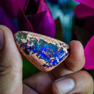 May include: A blue, green, and copper opal gemstone with a rough, natural shape. The opal is iridescent and has a variety of colors.