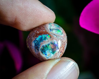 May include: A polished, rounded boulder opal gemstone featuring a textured, earthy brown matrix with three distinct, recessed cavities revealing vibrant, iridescent flashes of blue, green, and purple play-of-color with dark inclusions.