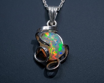 May include: A silver pendant necklace featuring a polished, iridescent opal gemstone with vibrant flashes of green, orange, and blue. The opal is encased in a swirling, sculptural silver metal setting that wraps around the stone, suspended from a chain.