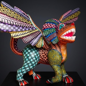 May include: A hand-painted alebrije sculpture of a mythical creature with wings, featuring a vibrant colour palette of orange, teal, yellow, and purple. The body is covered in intricate geometric patterns, including diamonds, swirls, and dots, with a wide-open mouth showing white teeth.