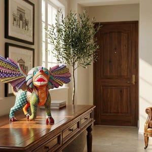 May include: A hand-painted wooden alebrije sculpture featuring a mythical creature with large, spread wings. The figure is decorated with intricate, colourful geometric patterns in shades of green, orange, purple, and yellow, with a wide, open mouth.