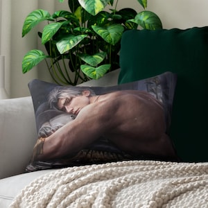 Könnte beinhalten: Ein rechteckiges Dekokissen mit einem aufgedruckten Bild einer oberkörperfreien Person mit hellem Haar, die den Kopf auf den Arm stützt. Das Kunstwerk zeigt eine dunkle, stimmungsvolle Farbpalette mit weichem Licht, das den Rücken und die Schulter betont.