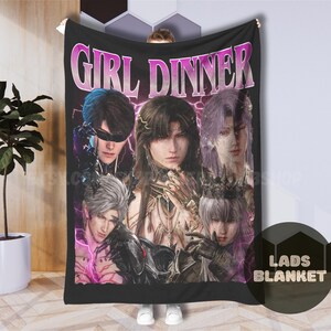 Può includere: Coperta nera con una grafica di cinque personaggi in stile anime con capelli lunghi e abiti ornati. La coperta ha il testo "GIRL DINNER" in rosa e bianco. La coperta è tenuta da una persona.