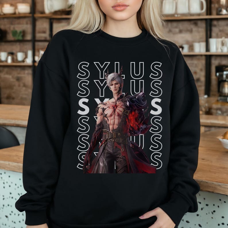 K&ouml;nnte beinhalten: Ein schwarzes Langarm-Sweatshirt mit einem Grafikdruck eines m&auml;nnlichen Charakters mit wei&szlig;em Haar und dunkler R&uuml;stung. Der Name SYLUS ist in wei&szlig;en vertikalen Textspalten hinter dem Charakter wiederholt, der ein rotes Emblem tr&auml;gt.