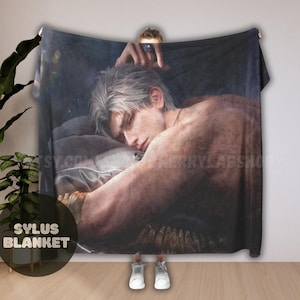 Peut inclure: Une grande couverture rectangulaire avec une illustration détaillée d'une personne aux cheveux argentés, reposant sur un oreiller. La couverture a un fond sombre et le texte "SYLUS BLANKET" est visible en bas à gauche.
