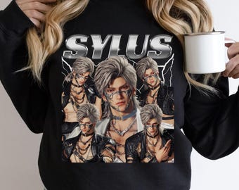 May include: A black crewneck sweatshirt featuring a graphic print with the text SYLUS in a metallic font. The design includes five overlapping portraits of a character with silver hair, wearing a black leather jacket and intricate silver chains.
