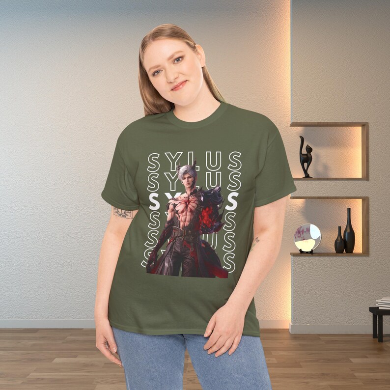 K&ouml;nnte beinhalten: Ein olivgr&uuml;nes T-Shirt mit einem Grafikdruck eines m&auml;nnlichen Charakters mit wei&szlig;em Haar und dunkler Kleidung. Das Wort SYLUS ist in wei&szlig;em, vertikalem Text hinter dem Charakter wiederholt. Das T-Shirt hat kurze &Auml;rmel und einen Rundhalsausschnitt.