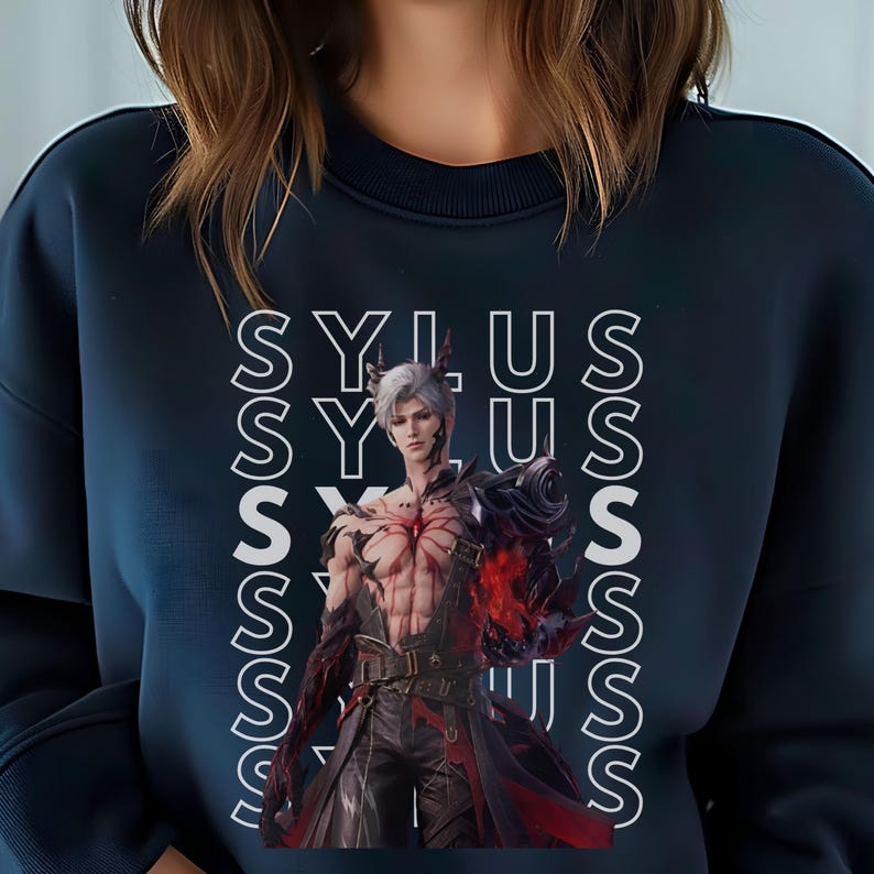 K&ouml;nnte beinhalten: Ein dunkelblaues Sweatshirt mit Rundhalsausschnitt und einem sich wiederholenden vertikalen wei&szlig;en Textmuster des Wortes SYLUS. Mittig auf der Vorderseite befindet sich eine Grafik eines silberhaarigen Charakters mit roten Markierungen.