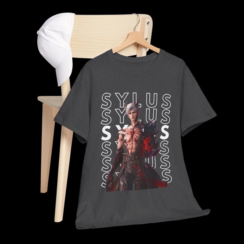 K&ouml;nnte beinhalten: Ein dunkelgraues Kurzarm-T-Shirt mit einem Grafikdruck eines m&auml;nnlichen Charakters mit wei&szlig;em Haar und roten Markierungen auf der Brust. Das Wort SYLUS ist in wei&szlig;en vertikalen Spalten hinter dem Charakter wiederholt. Eine wei&szlig;e Baseballkappe.