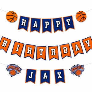 May include: A basketball-themed birthday banner set featuring three strings of pennants. The top string displays the word HAPPY in white letters on blue flags with basketballs at each end. The middle string spells BIRTHDAY in white on orange flags. The bottom string features the name JAX in white on blue flags, flanked by two New York Knicks team logos.