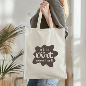 May include: A white canvas tote bag with brown text that reads "a little dirt never hurt!" The text is in a stylized font and is surrounded by a brown splotch.