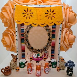 May include: A miniature Day of the Dead altar with orange roses, a yellow banner, and a decorative frame. The altar features miniature food, drinks, and skull figurines. The altar is decorated with colorful details and is a festive representation of the holiday.