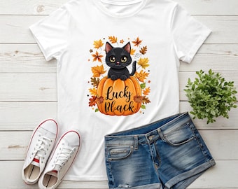 May include: White t-shirt with a black cat on an orange pumpkin, the text reads "Lucky Black". The design includes autumn leaves. The image also shows denim shorts and white trainers.