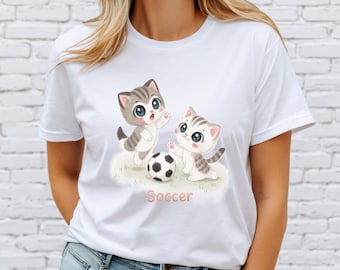 Op de afbeelding: Wit T-shirt met een afbeelding van twee cartoonkatten die voetbal spelen. De tekst "Soccer" is onder de katten gedrukt.