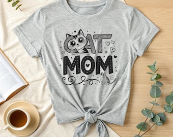 Puede incluir: Camiseta gris de manga corta con una ilustración en blanco y negro de un gato y el texto "CAT MOM" con corazones y espirales.