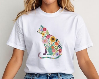 May include: White t-shirt featuring a colorful floral cat design. The cat silhouette is filled with various flowers in shades of pink, yellow, orange, and blue. The cat is sitting with its tail curled. The shirt has short sleeves and a crew neck.