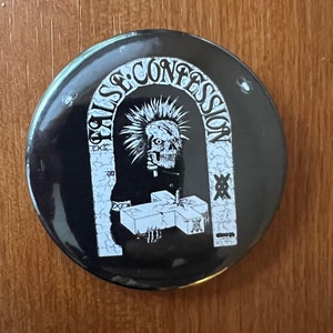 May include: Black and white button with a skull wearing a priest's collar holding a cross. The text "False Confession" is written in an arch above the skull.