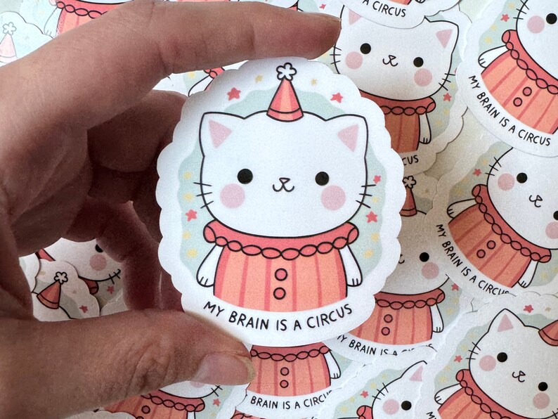May include: A white cat wearing a red and white clown costume with a party hat. The cat has pink cheeks and black eyes. The text "My brain is a circus" is written below the cat.