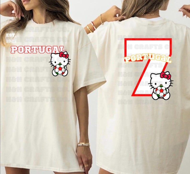 K&ouml;nnte beinhalten: Cremefarbenes T-Shirt mit dem Wort "PORTUGAL" in Rot, einem Hello Kitty-Motiv mit einem Fu&szlig;ball und der Zahl "7" auf dem R&uuml;cken. Das Shirt hat eine lockere Passform und kurze &Auml;rmel. Der Text "EST 192" ist ebenfalls sichtbar.